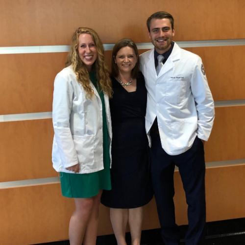 2 med school students wearing new white coats and director in middle