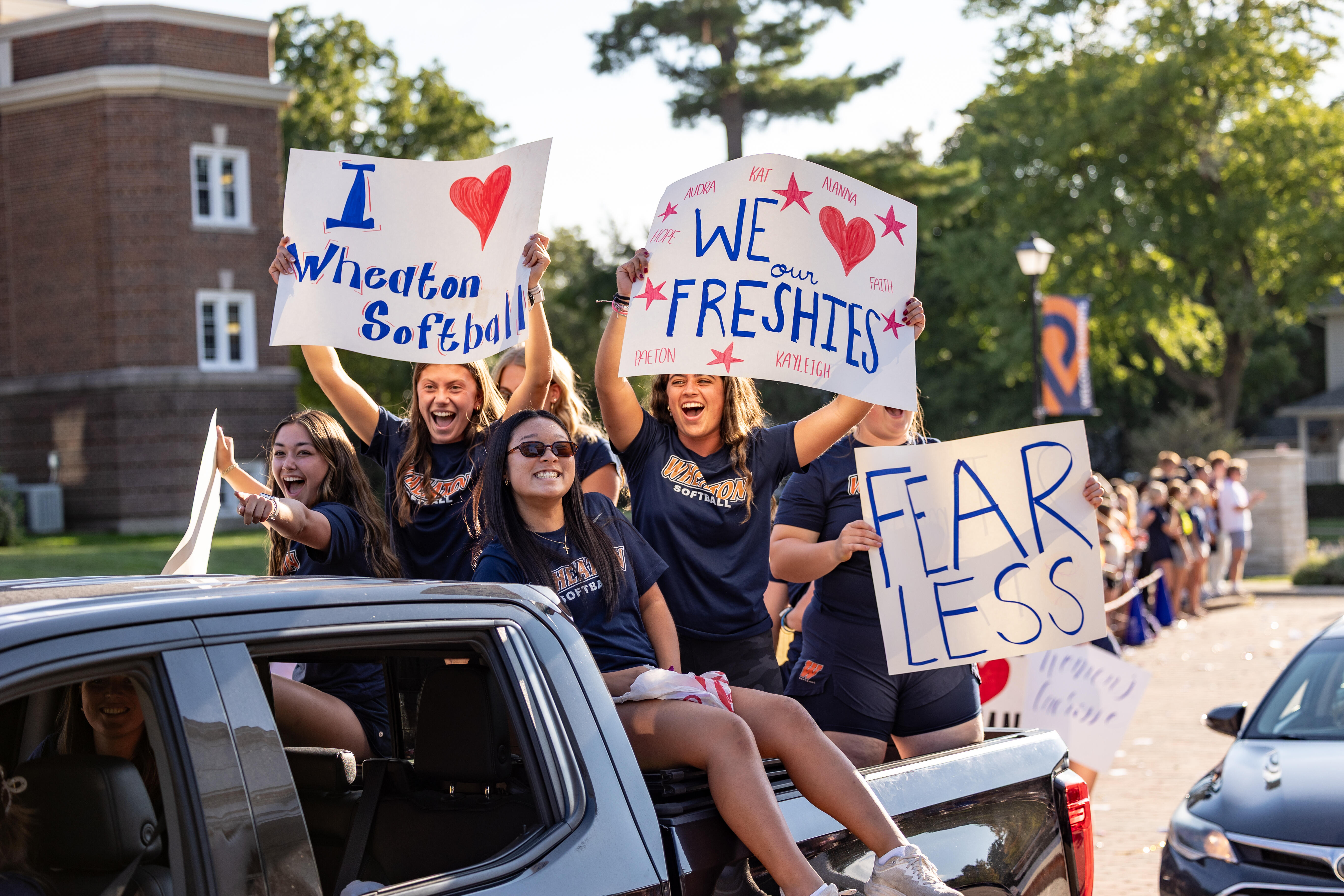 Wheaton Students riding in truck with "We Love Freshies" signs
