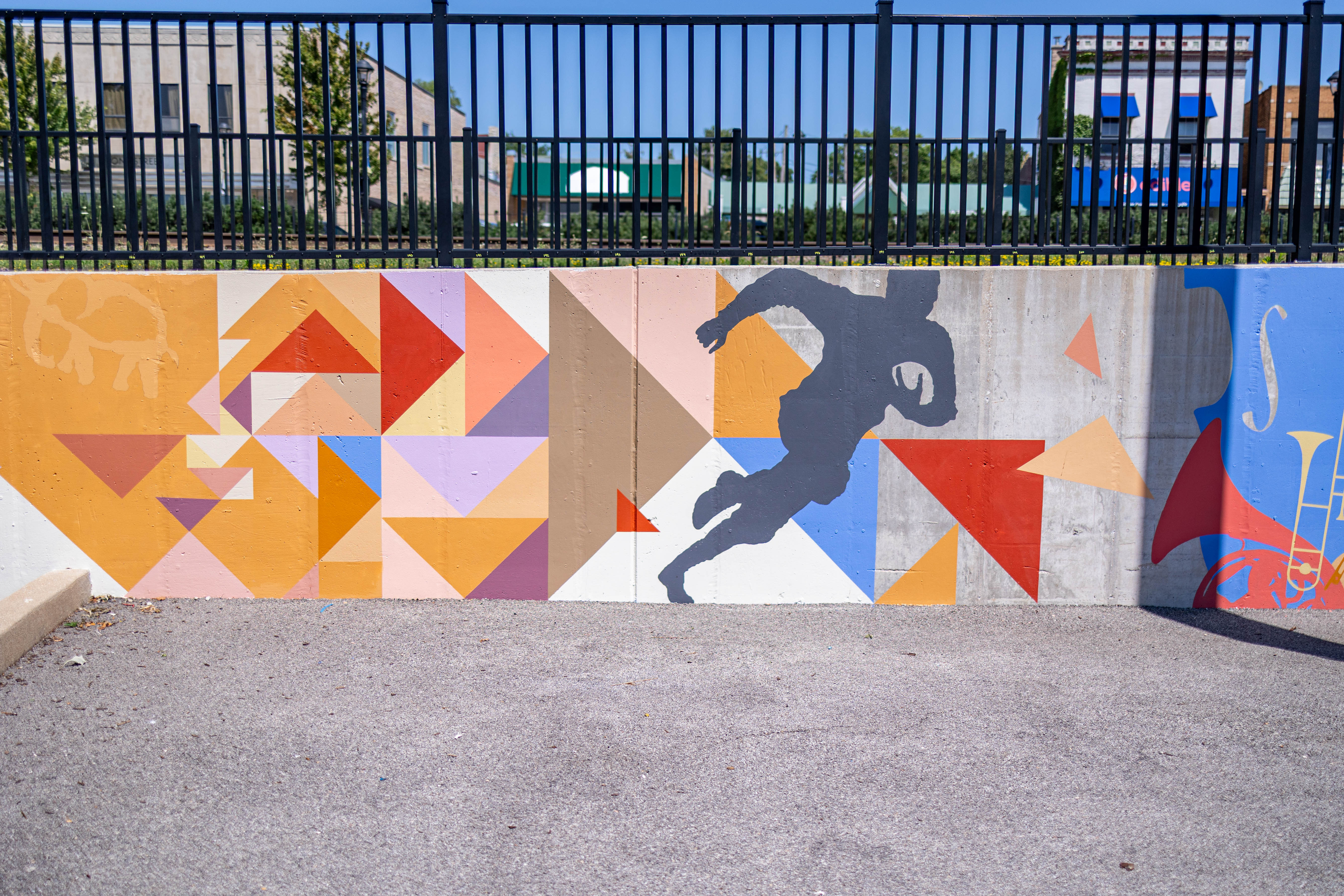 An outdoor wall that has colorful shapes and a running man painted on it.
