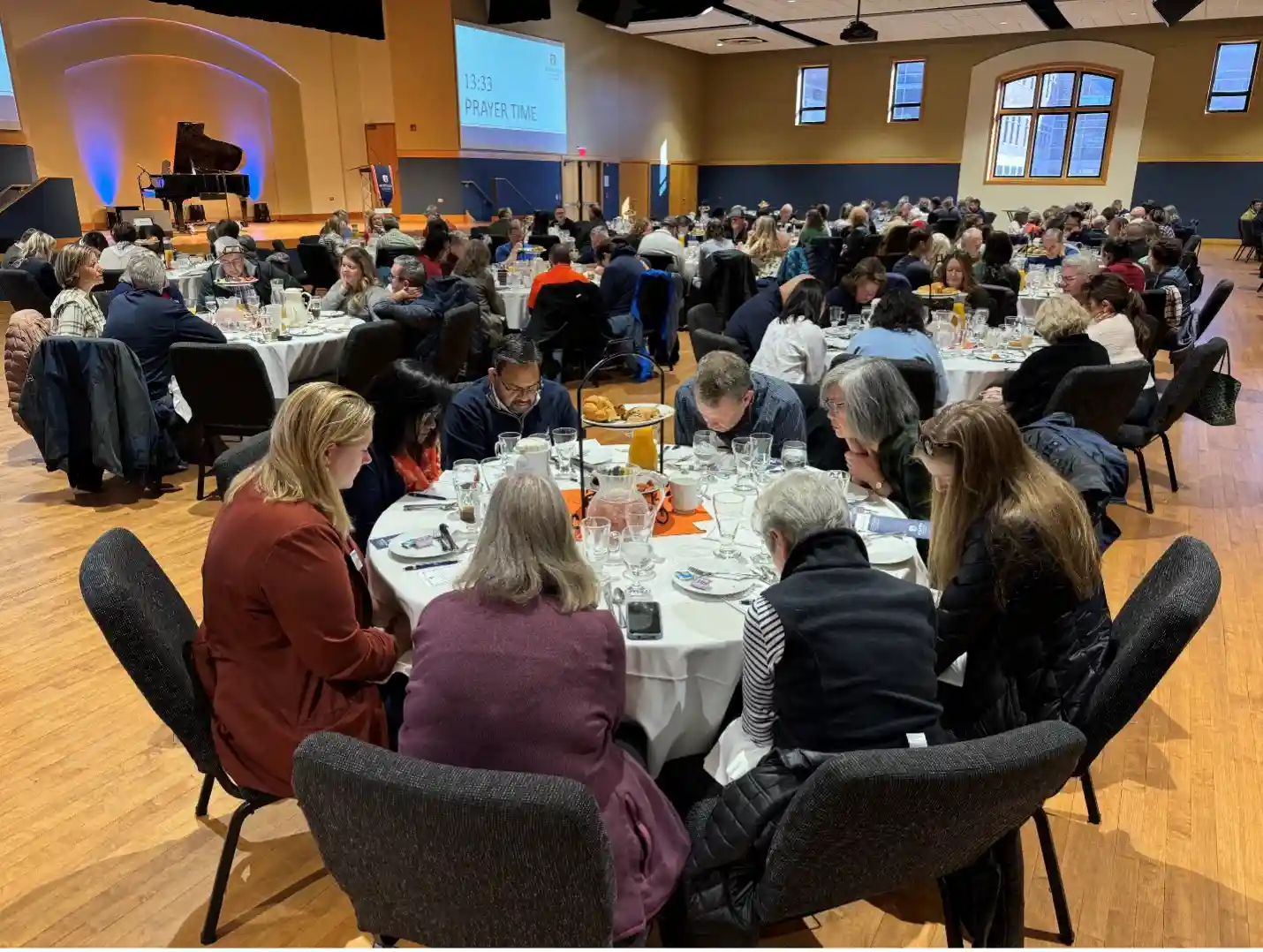 A big group of people sitting at round tables, praying together