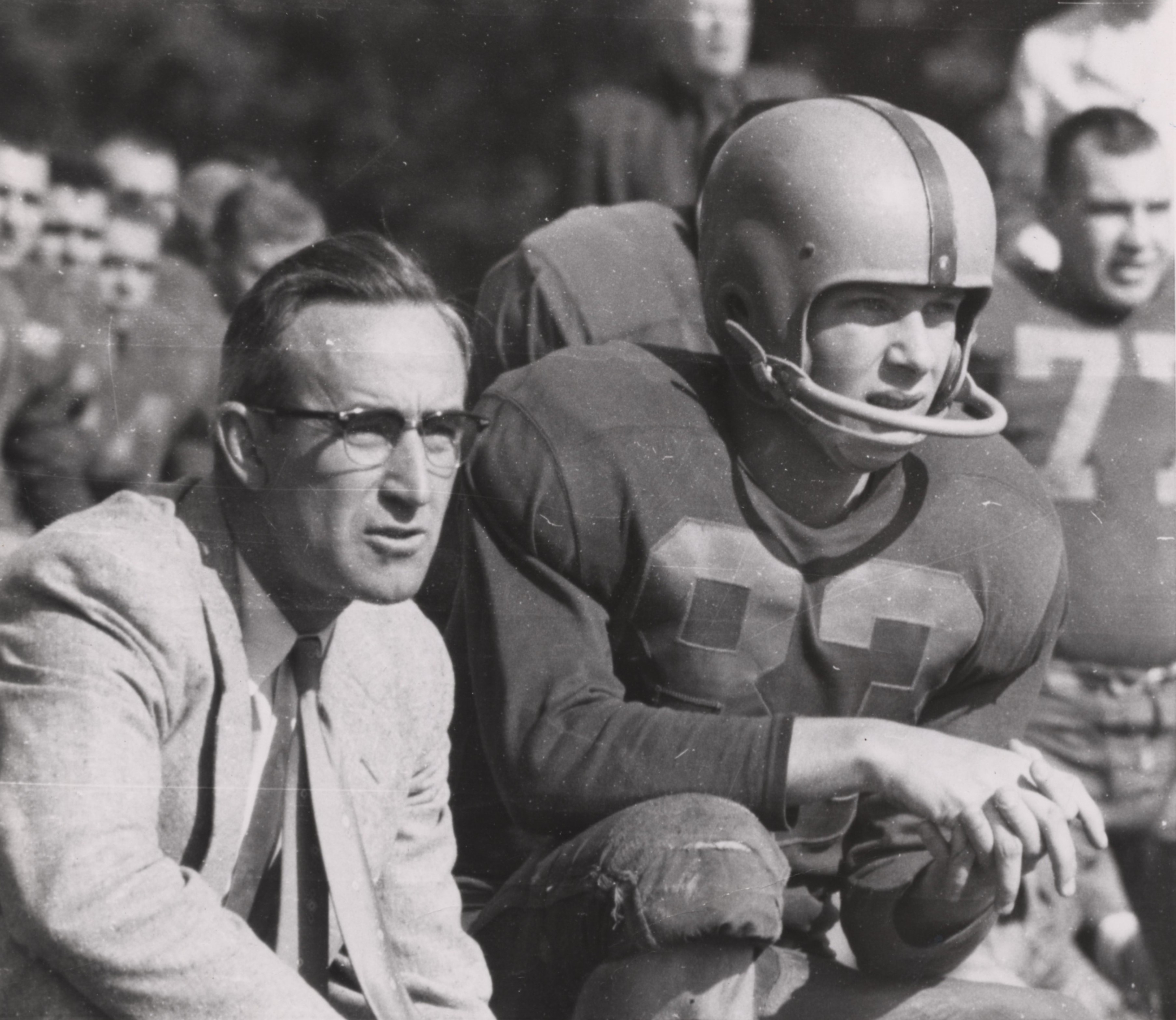 3614x3134 Harve Chrouser with a football player A man in a suit squats next to a man in a football uniform.
