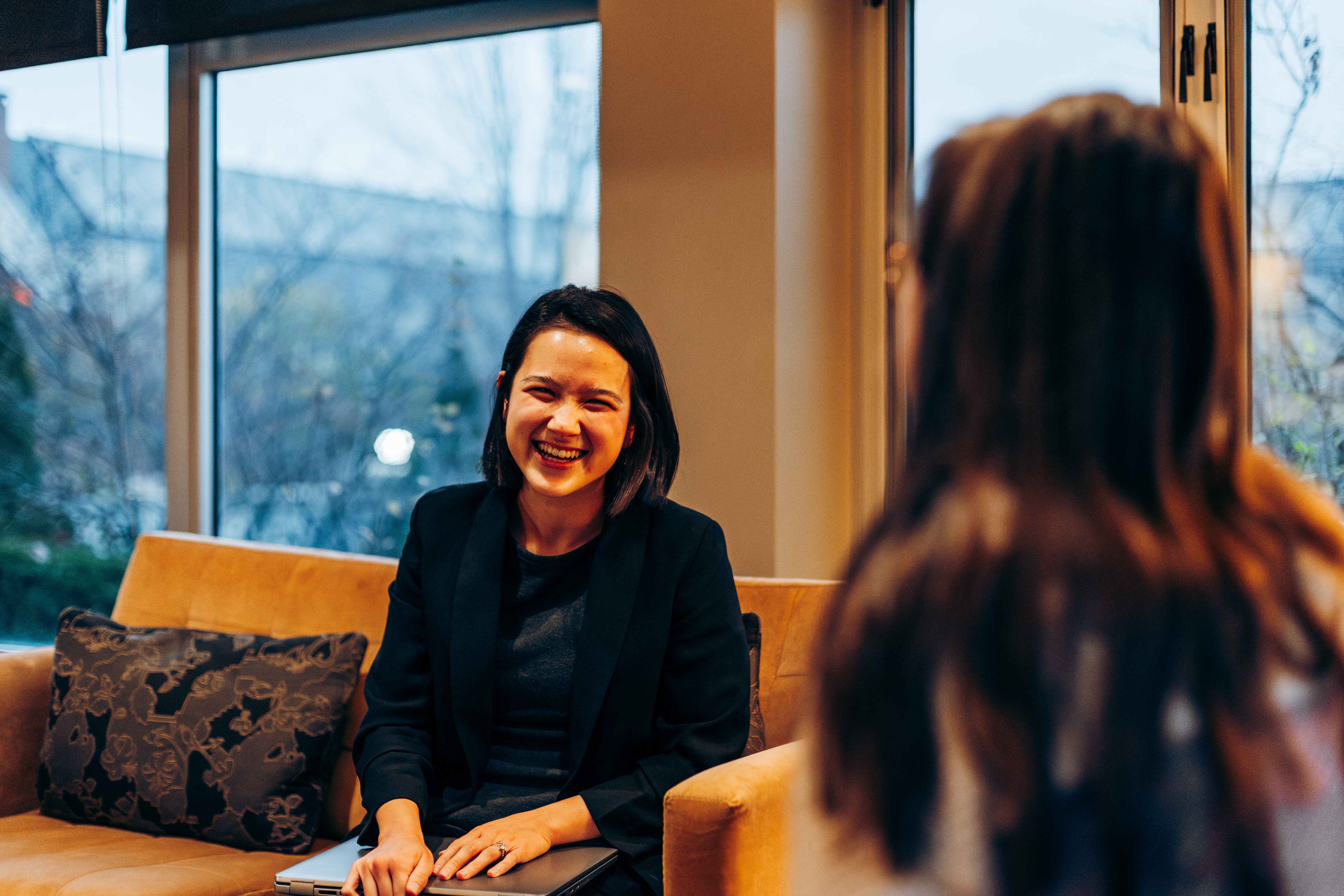 Woman in a blazer smiling on a couch
