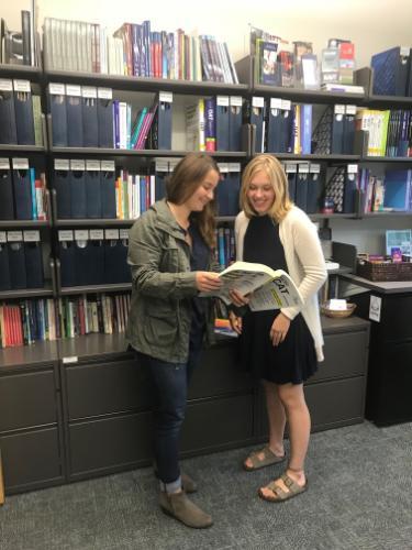 2 female students looking at an open book in front of the Resource Center library