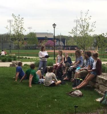 students sitting on grass listening to professor