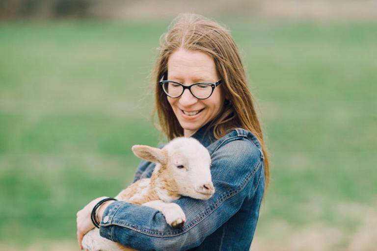 Wheaton College IL English professor Dr. Tiffany Kriner caring for sheep and holding a lamb at Root and Sky Farm