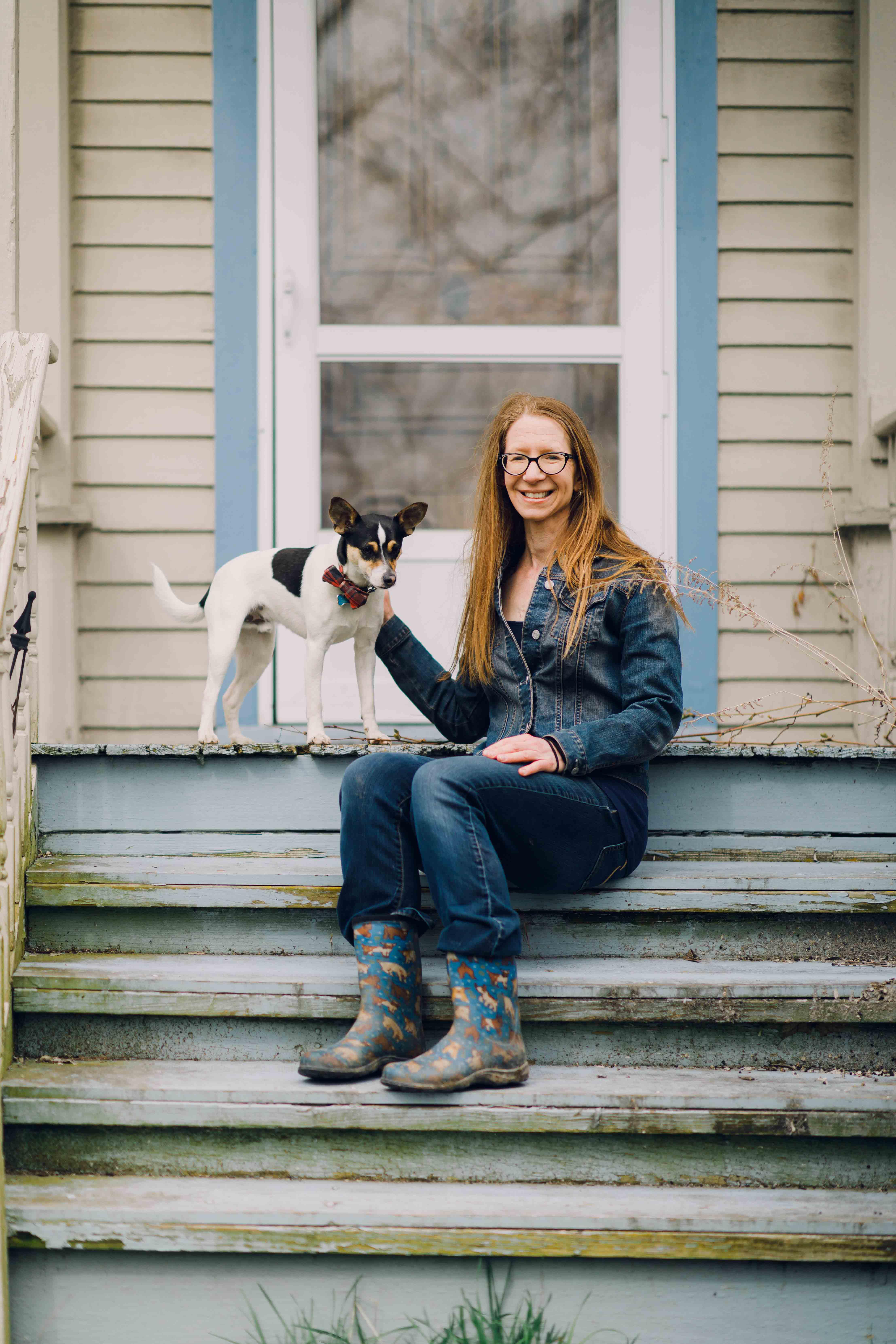 Wheaton College IL English professor Dr. Tiffany Kriner sitting on the stoop of her farmhouse with a spotted dog