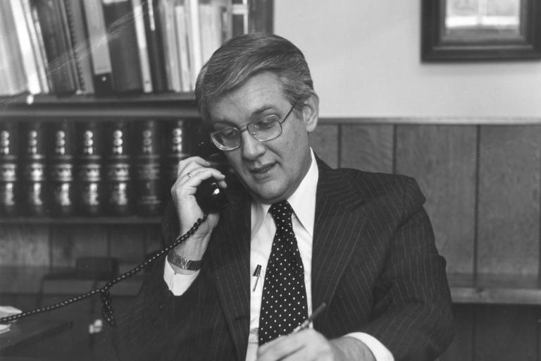 Dr. Bill Pollard wearing a suit and taking notes while on the phone in his office