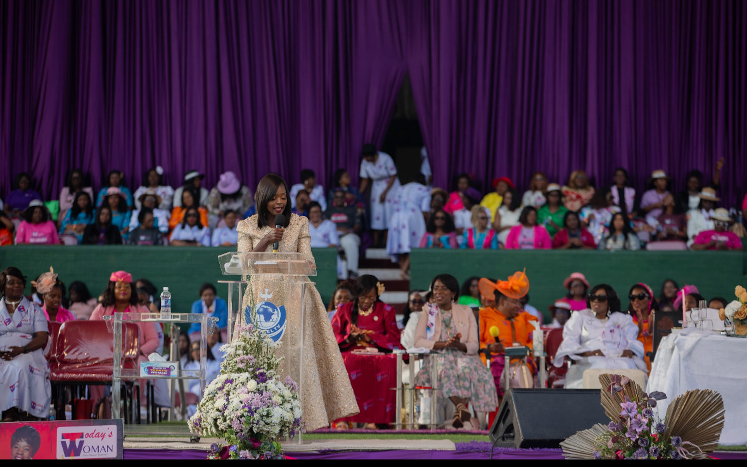 An African woman in a sparkly dress speaks to a large audience
