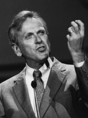 A black and white photo of a white man speaking from a podium with a microphone
