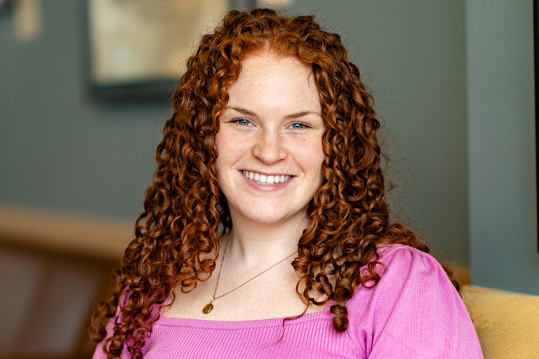 A young woman with curly auburn hair smiles