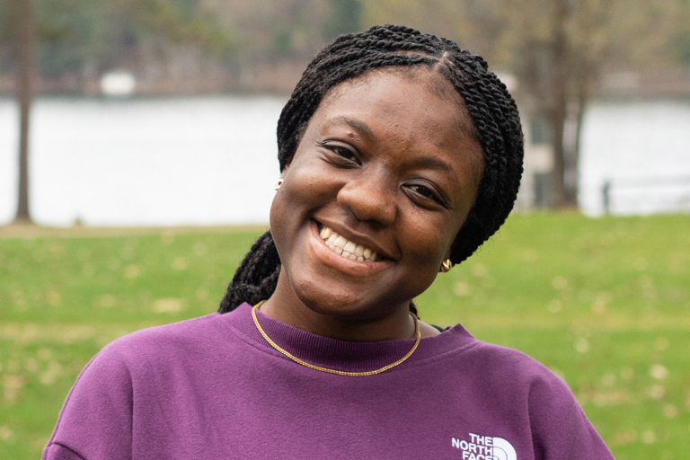 A black woman stands in front of a lake and smiles