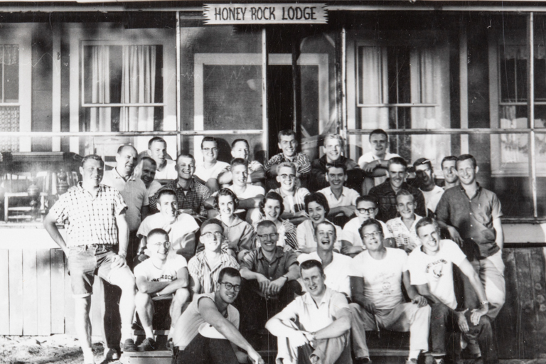 A black and white photo of a group of men and women in front of a building labeled Honey Rock Lodge