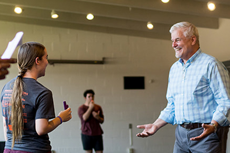A white-haired man speaks to a female student
