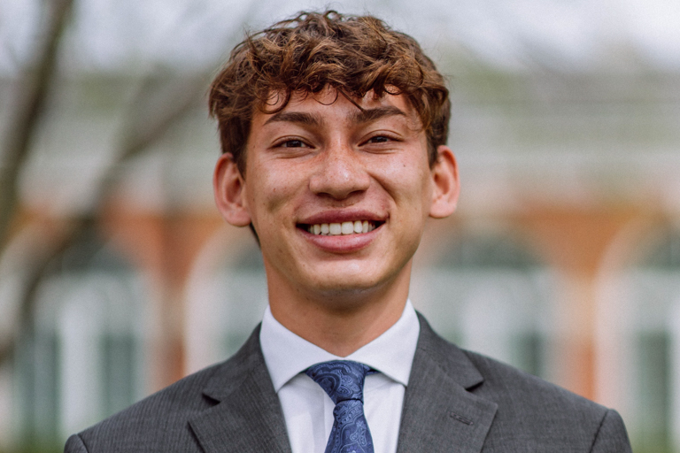 A young man with brown curly hair smiles