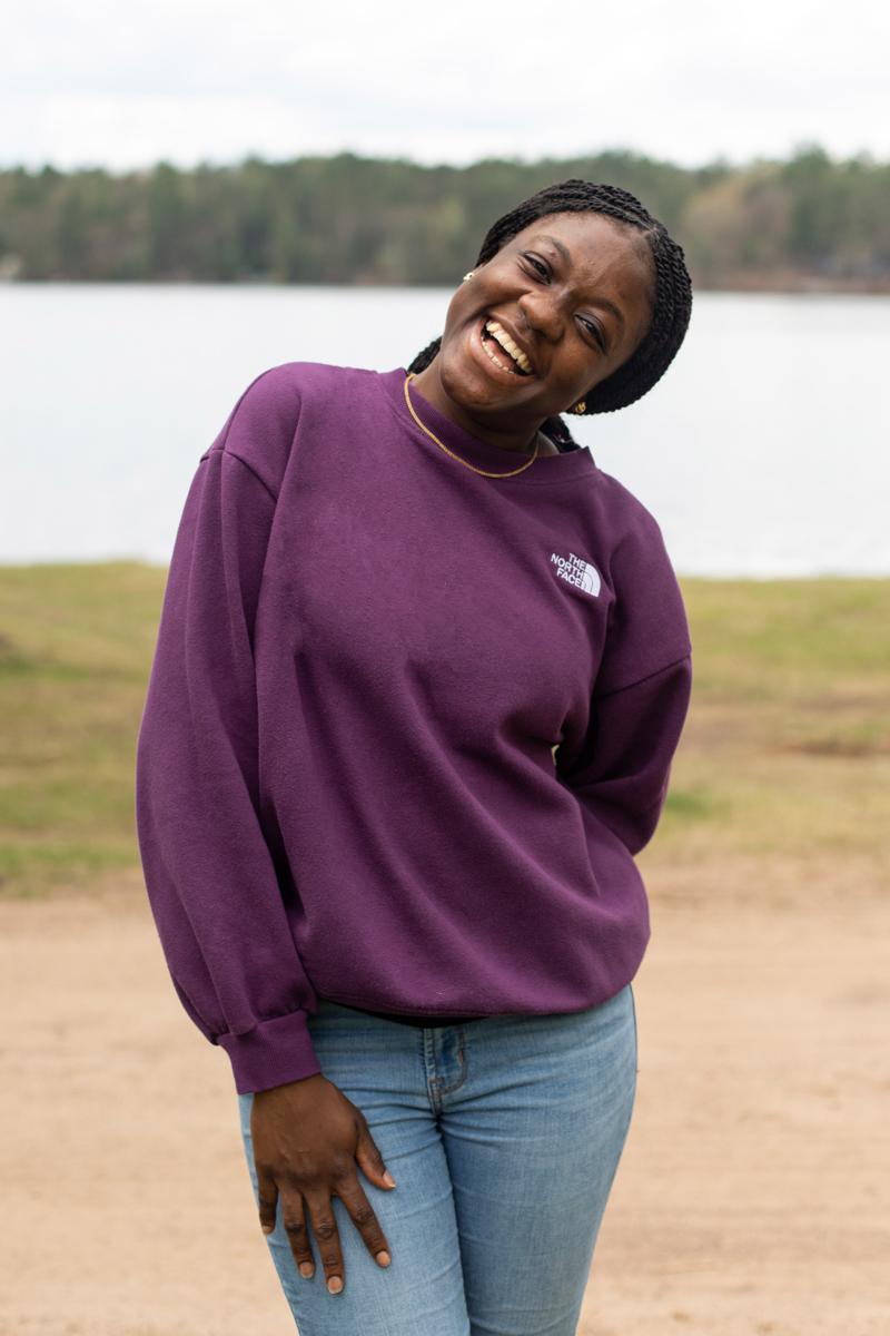 A black woman stands in front of a lake and smiles