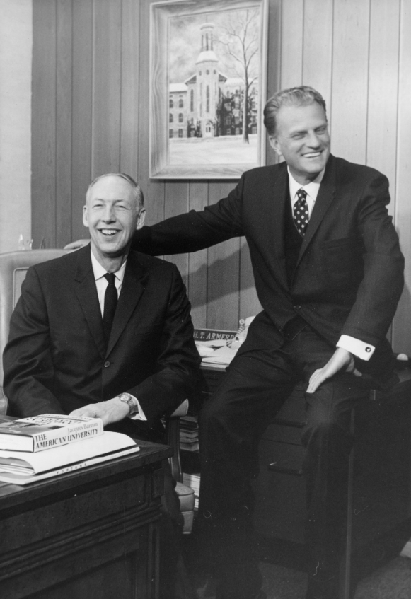 A black and white photo of two white men sitting next to each other and smiling