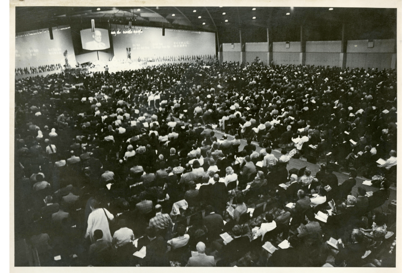 A black and white photo of an audience facing a stage lined with flags from different countries