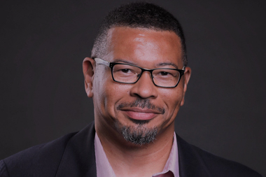 A black man wearing glasses smiles
