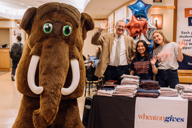 Two female college students and a male college president stand next to a mastodon mascot