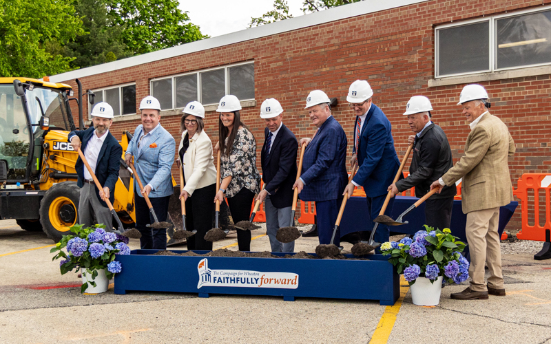 A group of men and women holding shovels smile