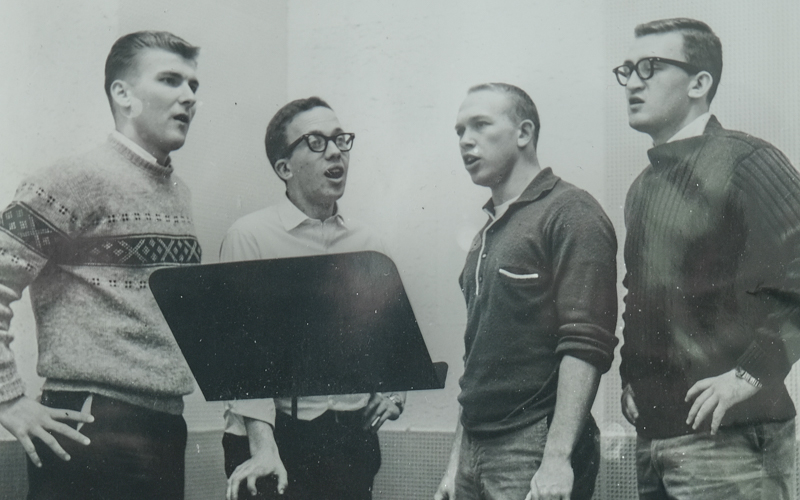 A black and white photo of four young white men singing in a recording booth