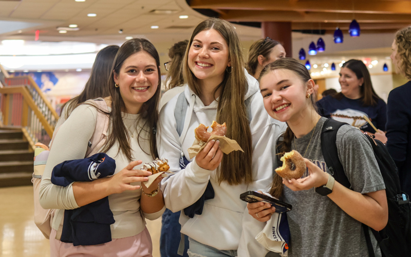 three young white woman smile and hold donuts